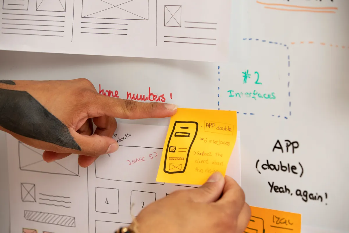Hands pointing at UX wireframes and sticky notes for design planning